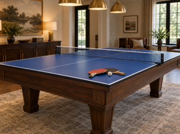 Blue table tennis conversion top and net over a wood pool table, with paddles and a ball.